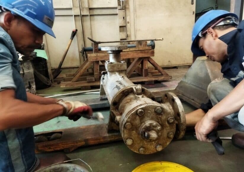 Dua teknisi membongkar rumah pompa untuk direkondisi di bengkel